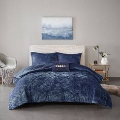 a bed with blue comforter and pillows in a room next to a painting on the wall