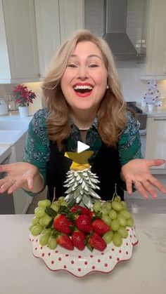 a woman standing in front of a cake decorated like a christmas tree with fruit on it