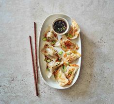 a white plate topped with dumplings next to two chopsticks and a dipping sauce