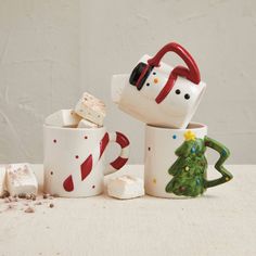 three coffee mugs with marshmallows and candy canes on the side