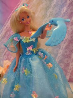 a barbie doll with a blue dress and bird on her arm, in front of a pink background