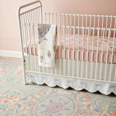 a white crib with pink and blue bedding next to a rug on the floor