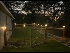 some lights that are on the side of a house near a fence and grass field