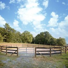 a fenced in area with grass and trees on the other side, surrounded by blue skies