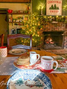 a table with plates and cups on it in front of a fireplace decorated for christmas