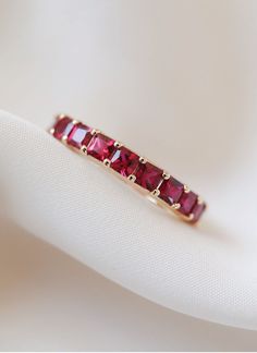 a close up view of a ring with red stones on it's side, sitting on a white cloth