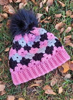 a pink and black knitted hat laying on top of leaves