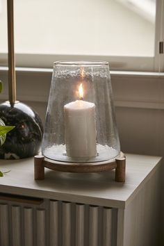 a white candle sitting on top of a wooden stand next to a window sill