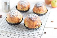 four muffins on a cooling rack next to an apple and cinnamon shaker