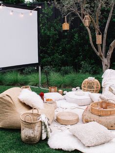 an outdoor movie is set up on the grass in front of a large screen and wicker baskets