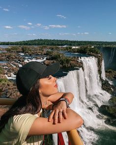 a woman standing next to a waterfall and looking up at the sky with her arms crossed