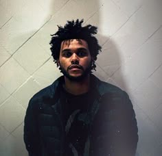 a man with dreadlocks standing in front of a white wall and looking at the camera