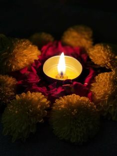 a lit candle surrounded by flowers on a black surface with red and yellow petals around it