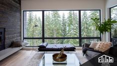 a living room with couches, coffee table and large windows overlooking the trees outside