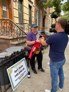 two people standing on the sidewalk with a red ribbon around their necks and one person holding a camera