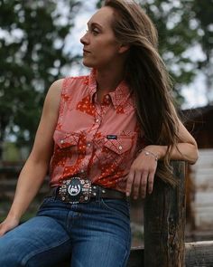 a woman with long hair sitting on a wooden post wearing a red shirt and jeans