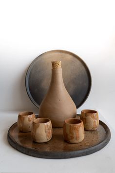 a brown vase sitting on top of a wooden tray next to small cups and saucers