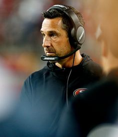 a close up of a coach wearing headphones on the sidelines during a football game