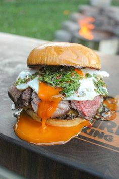 a burger with meat, cheese and sauce on it sitting on top of a wooden table