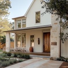 a white house with two brown doors and some plants in the front yard on a sunny day