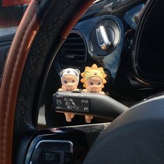 two small figurines sitting in the center console of a car with steering wheel controls