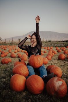 a woman sitting in a field full of pumpkins with her arms up and smiling