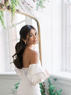 a woman standing in front of a mirror wearing a white dress with ruffled sleeves