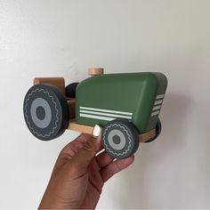 a hand holding a green toy truck on top of a white wall in a room