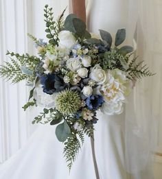 a bridal holding a bouquet of white and blue flowers with greenery on it