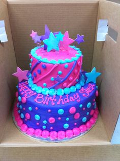 two tiered birthday cake in a box with stars on the top and pink, blue, and purple frosting