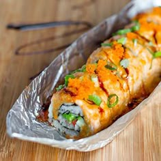 a piece of sushi wrapped in foil on a wooden table