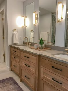 a bathroom with two sinks, mirrors and lights on the wall above them is shown