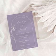 the wedding card is laying on top of a white cloth with an elegant design and flowers