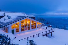 a ski lodge is lit up at night on a snowy mountain top with the ocean in the background