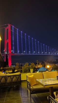 people are sitting at tables in front of a bridge with bright lights on the side