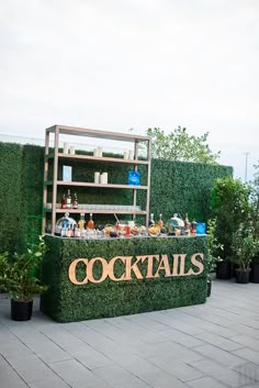 a sign that says cocktails on it in front of some plants and potted trees