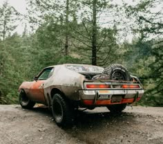 an old rusted out car is parked in the dirt near some trees and rocks