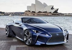 a blue sports car parked in front of the sydney opera house with water behind it