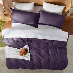 a bed with purple and white comforters on top of it next to a potted plant