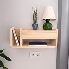 a wooden shelf with two books on it next to a lamp and potted plant