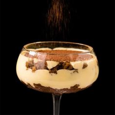 a dessert in a glass on a black background is being sprinkled with chocolate