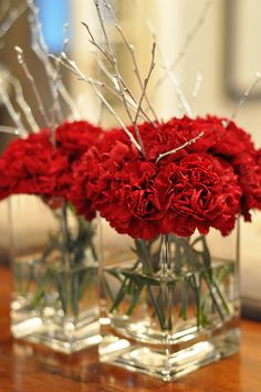 two clear vases filled with red flowers on top of a wooden table