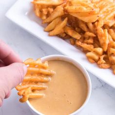 a person dipping some fries into a small white bowl filled with sauce on the side