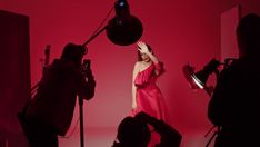 a woman in a red dress is holding her hands up to the sky while she stands behind a camera