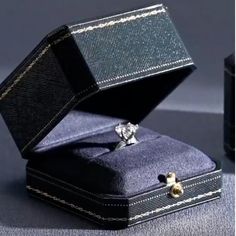 an open black box with a ring in it sitting on top of a blue surface