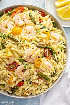 pasta with shrimp and asparagus in a bowl next to lemon wedges on the side