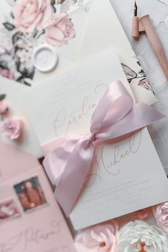 the wedding stationery is laid out with pink flowers and ribbons on it's side