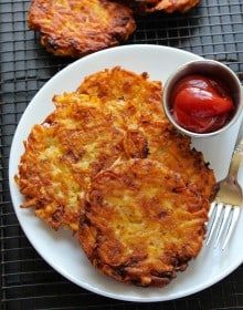 a white plate topped with hash browns next to a fork and cup of ketchup