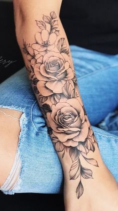 a woman's arm with roses and leaves tattooed on the side of her leg