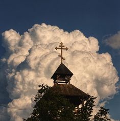 a church steeple with a cross on top and clouds in the background